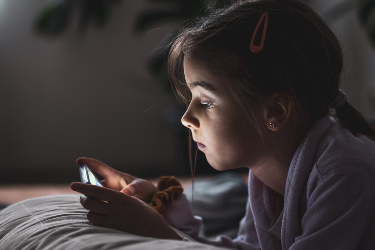 Función de las mentiras en los niños: ¿por qué los niños mienten? Una niña utiliza un smartphone tumbada en la almohada de su casa.